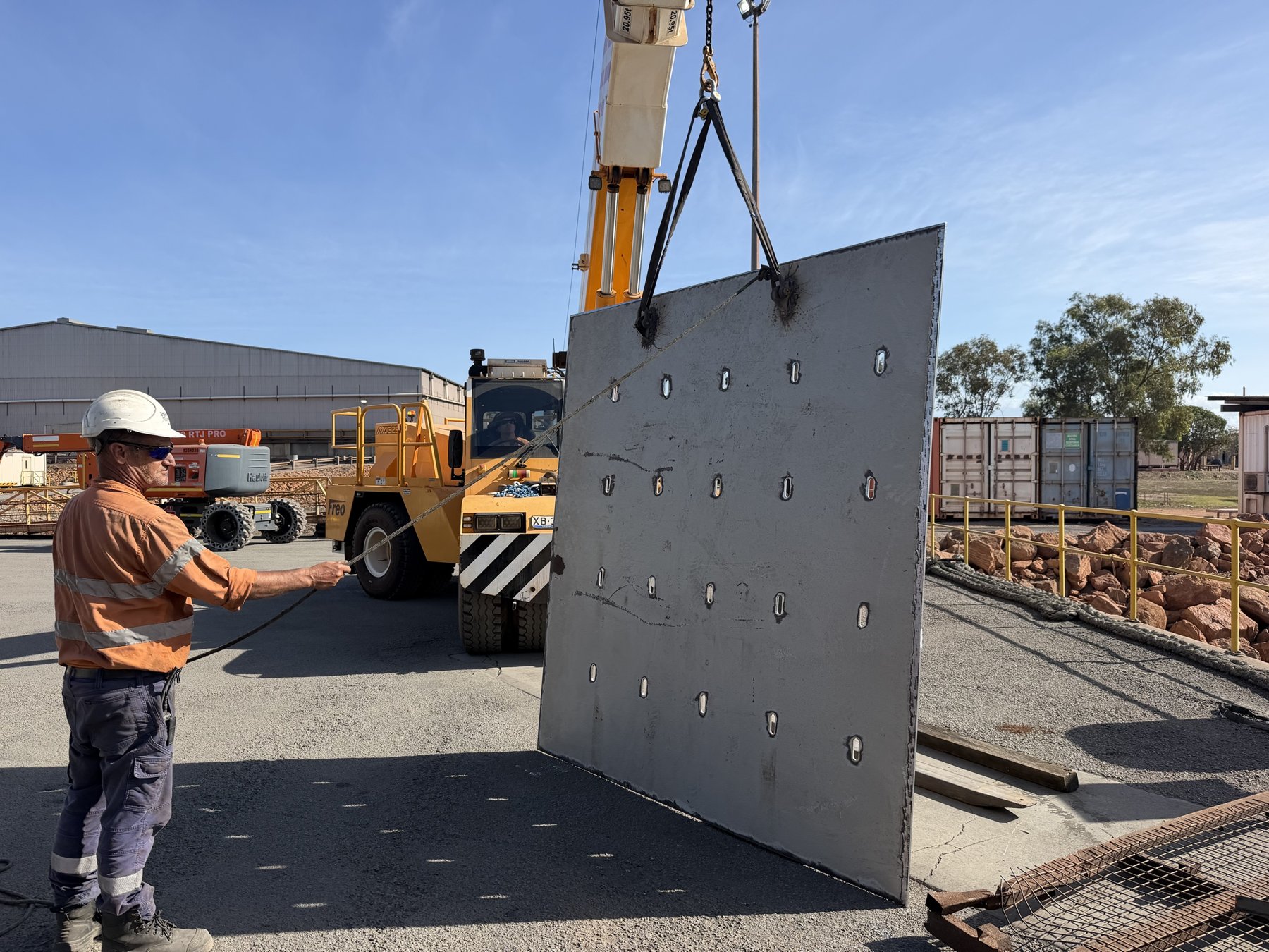 Crane lifting a slotted 2 by 3 metre hull doubler plate on the wharf at Bing Bong with a rigger holding a tag line