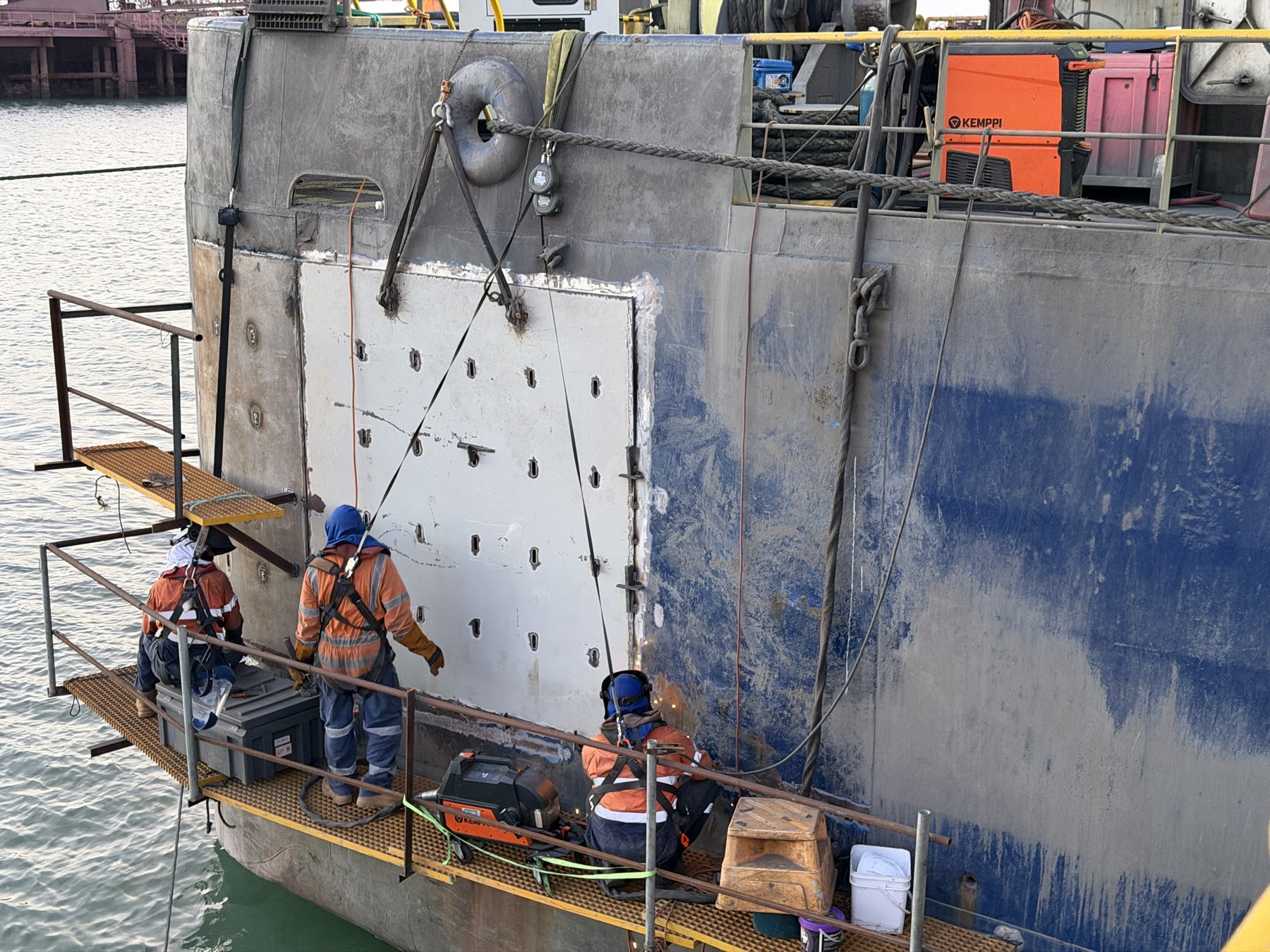 Qualships welders on temporary welded work platforms fitting a hull doubler plate to the ship's side above the water