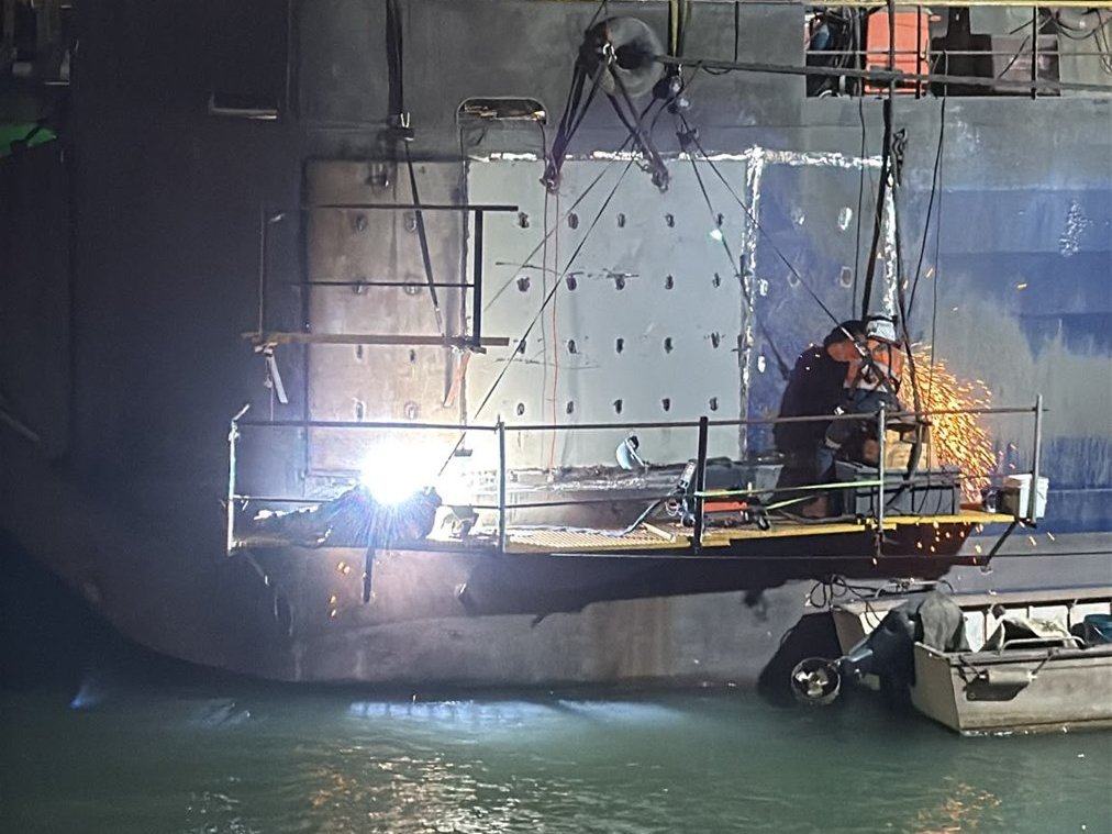 Welder working at night under floodlights on the ship's side at Bing Bong, sparks flying from the work platform